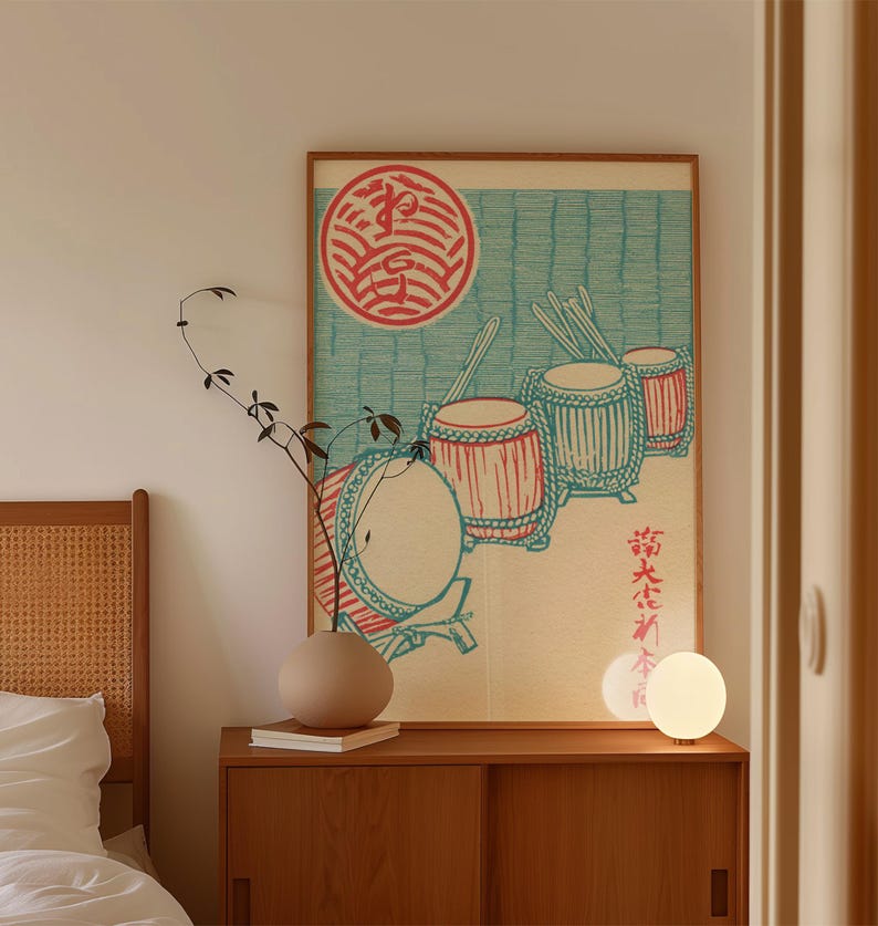 May include: A framed print featuring Japanese drums in red and teal against a light blue background. The artwork includes a red circular emblem and Japanese text. The print is displayed above a wooden cabinet with a vase and a lamp.