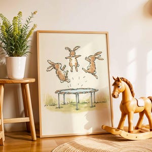 May include: A framed print featuring three cartoon rabbits jumping on a trampoline. The artwork is in a light wood frame, and a wooden rocking horse and a small stool with a plant are in the foreground. The scene is set in a child's room.