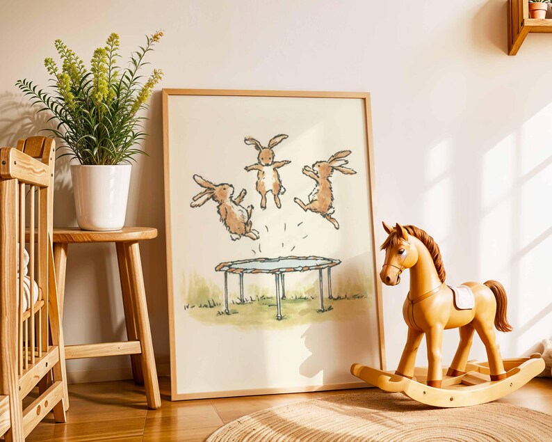 May include: A framed print featuring three cartoon rabbits jumping on a trampoline. The artwork is in a light wood frame, and a wooden rocking horse and a small stool with a plant are in the foreground. The scene is set in a child's room.