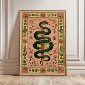 Op de afbeelding: Ingelijste kunstdruk met een groene slang die zich rond een gouden staf wikkelt, tegen een roze achtergrond met bloemen en botanische elementen. Het kunstwerk is ingelijst in een houten frame.