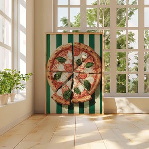 May include: A framed pizza art print featuring a sliced pizza with tomatoes, mozzarella, and basil. The pizza is set against a green and white striped background. The artwork is displayed in a room with a window and plants.