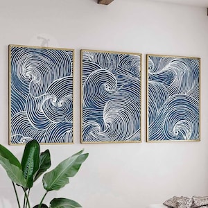 May include: Three framed abstract art pieces. Each features a navy blue background with white swirling lines, creating a wave-like pattern. The frames are gold-colored, and the artwork is displayed on a white wall.