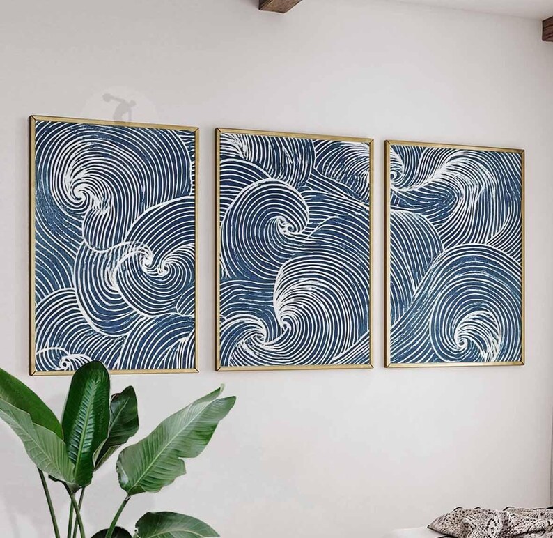 May include: Three framed abstract art pieces. Each features a navy blue background with white swirling lines, creating a wave-like pattern. The frames are gold-colored, and the artwork is displayed on a white wall.