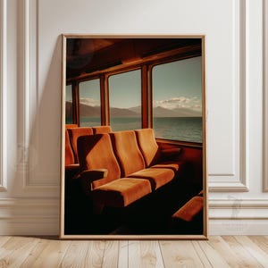 Può includere: Una stampa artistica incorniciata che raffigura l'interno di una carrozza ferroviaria con file di sedili in velluto arancione di fronte a grandi finestre che rivelano una vista su un mare calmo e montagne lontane, con il testo THE WORLD GALLERY.