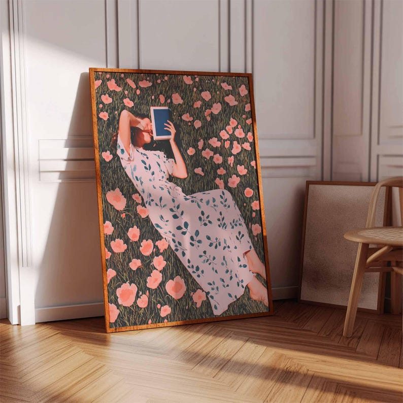 K&ouml;nnte beinhalten: Ein gerahmter Kunstdruck zeigt eine Person, die in einem Feld aus rosa Blumen liegt und ein blaues Buch h&auml;lt. Die Person tr&auml;gt ein hellrosa Kleid mit gr&uuml;nen Bl&auml;ttern. Das Kunstwerk befindet sich in einem Raum mit Holzboden und wei&szlig;er Wand.