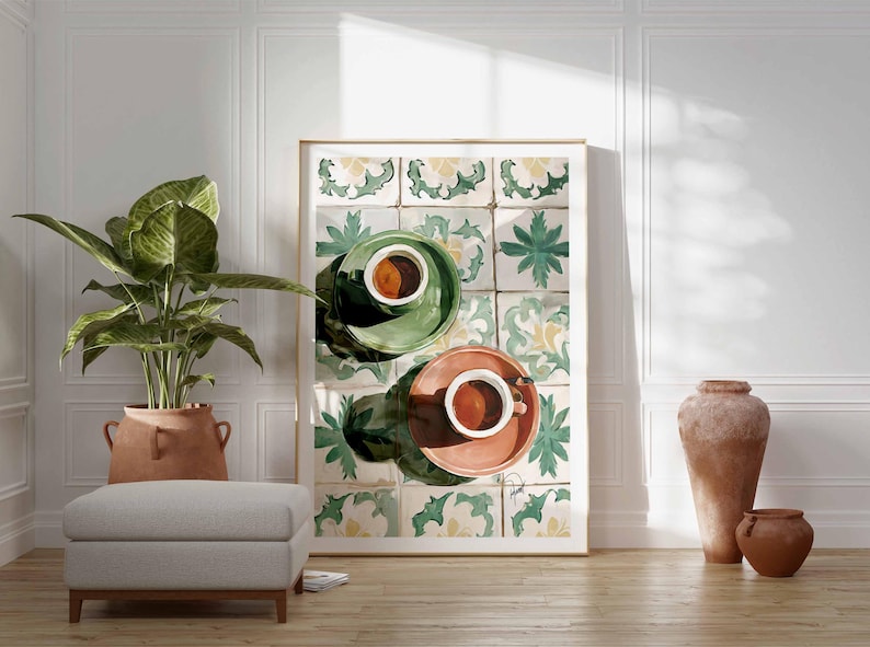 May include: A framed art print featuring two cups of coffee on saucers, one green and one coral, set against a backdrop of patterned tiles. The scene is in a bright room with a plant, ottoman, and decorative vases.