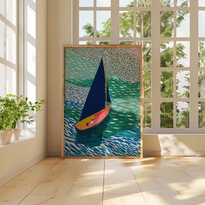 May include: A framed art print depicting a sailboat on water. The boat features a dark blue sail and a pink and yellow hull, set against turquoise and green water. The artwork is displayed in a bright room with a large window, with natural light.