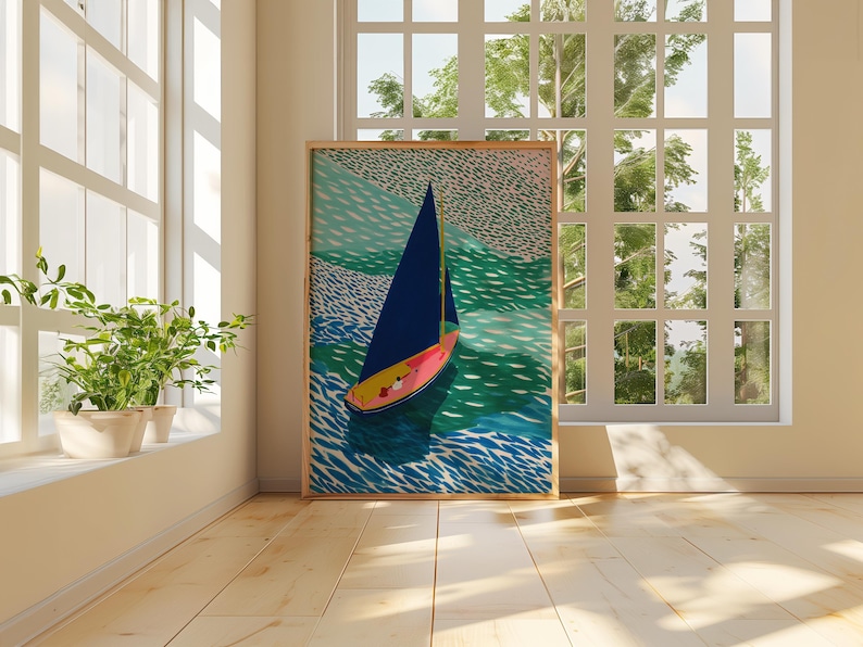 May include: A framed art print depicting a sailboat on water. The boat features a dark blue sail and a pink and yellow hull, set against turquoise and green water. The artwork is displayed in a bright room with a large window, with natural light.