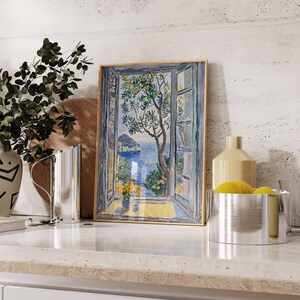 Puede incluir: Una pintura enmarcada de una ventana con vista a un oc&eacute;ano azul y una peque&ntilde;a isla. La ventana est&aacute; abierta y hay un &aacute;rbol verde en primer plano. La pintura est&aacute; sobre una encimera blanca con un jarr&oacute;n y una jarra.