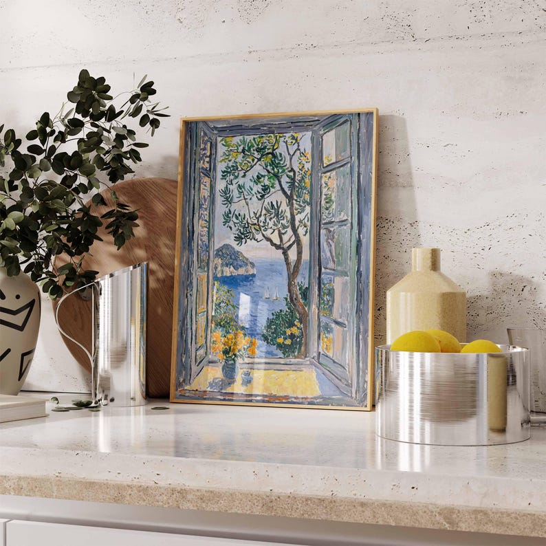 Puede incluir: Una pintura enmarcada de una ventana con vista a un oc&eacute;ano azul y una peque&ntilde;a isla. La ventana est&aacute; abierta y hay un &aacute;rbol verde en primer plano. La pintura est&aacute; sobre una encimera blanca con un jarr&oacute;n y una jarra.