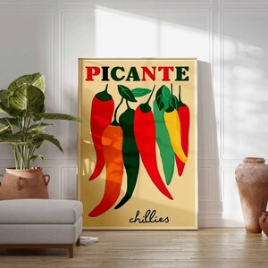 May include: A framed art print featuring a stylized illustration of chili peppers in red, orange, green, and yellow against a beige background. The word "PICANTE" is at the top in red letters, with "chillies" in black at the bottom.
