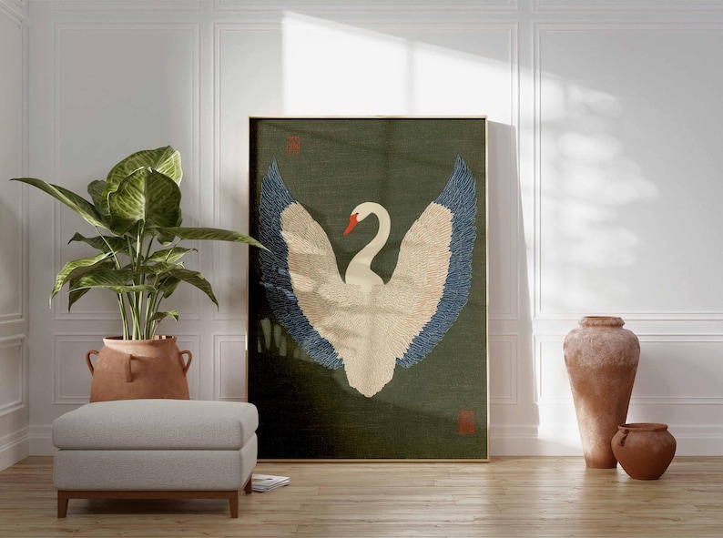 Pode incluir: Uma obra de arte emoldurada com um cisne branco com asas azuis e bege sobre um fundo verde escuro. A obra de arte &eacute; exibida em uma sala com uma planta em vaso, um pufe cinza e vasos de terracota. A sala tem pain&eacute;is brancos e um ch&atilde;o de madeira.