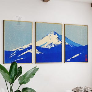 K&ouml;nnte beinhalten: Ein Triptychon gerahmter Kunstdrucke mit einer Berglandschaft in Blau- und Wei&szlig;t&ouml;nen. Das Kunstwerk hat eine Vintage-&Auml;sthetik mit hellblauem Himmel und schneebedeckten Gipfeln. Die Rahmen sind goldfarben, und der Text "THE WORLD GALLERY" ist sichtbar.