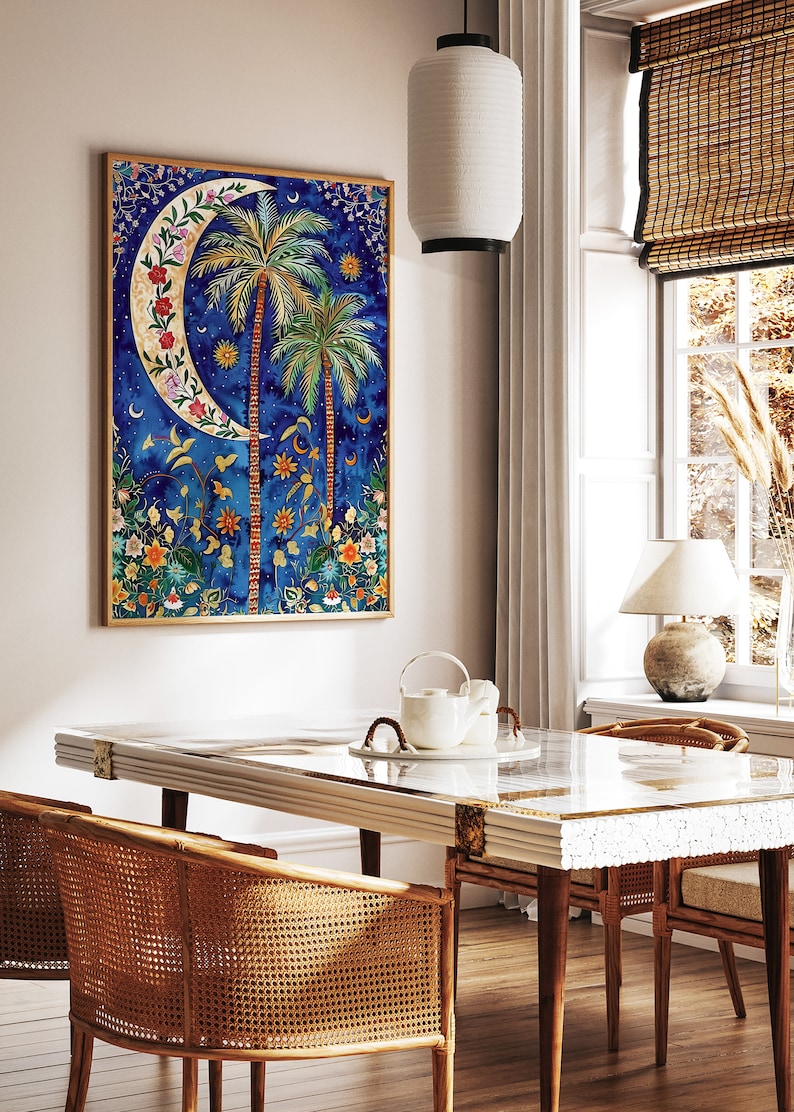 May include: A framed painting of a crescent moon with palm trees and flowers on a blue background. The painting is hanging on a white wall above a wooden table with two wicker chairs.