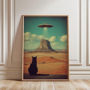 Könnte beinhalten: Gerahmter Kunstdruck mit einer schwarzen Katzen-Silhouette, die eine UFO über einer Wüstenlandschaft betrachtet. Das Kunstwerk hat eine Vintage-Ästhetik mit türkisfarbenem Himmel, Wolken und einer braun-orangenen Wüste.