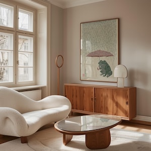 May include: A living room with a white, curved sofa, a wooden coffee table with a glass top, and a wooden cabinet. A framed artwork shows a green frog under an umbrella in the rain. A white lamp and a wooden floor lamp are also present.