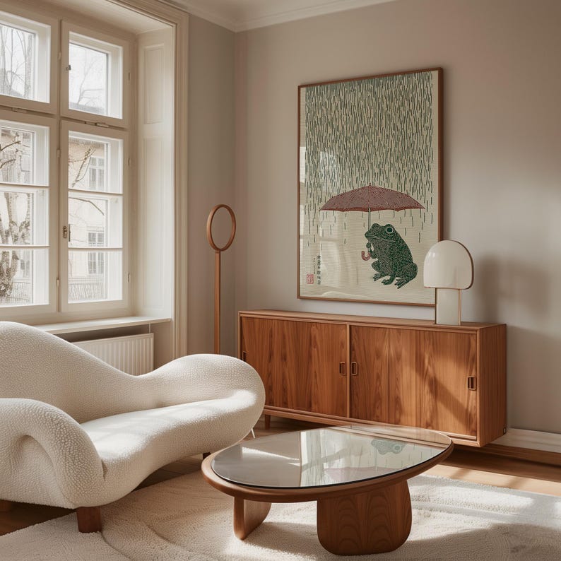 May include: A living room with a white, curved sofa, a wooden coffee table with a glass top, and a wooden cabinet. A framed artwork shows a green frog under an umbrella in the rain. A white lamp and a wooden floor lamp are also present.