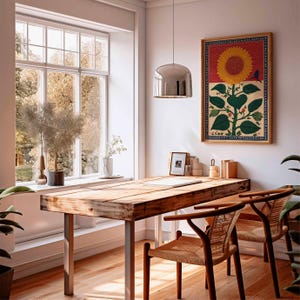 May include: A rustic wooden desk with metal legs and two woven chairs. A framed sunflower print hangs on the wall. The room has a large window with a view of trees and a silver pendant light.