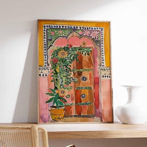 May include: A watercolor painting of a colorful doorway with a pink archway, a wooden door, and a potted plant. The door is decorated with green, blue, and yellow details. The painting is framed in a yellow frame.