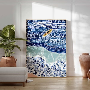 May include: A framed art print depicting a surfer on a surfboard in the ocean. The artwork features shades of blue and white to represent the water and waves. The print is displayed in a room with a plant, ottoman, and decorative vases.