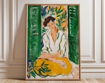 May include: A framed art print featuring a seated figure in a white shirt and yellow skirt. The painting has a green and orange background with foliage. The artwork is in a wooden frame and leans against a white wall.
