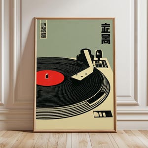 以下が含まれることがあります： レコードプレーヤーの様式化されたイラストが描かれた、額装されたアートプリント。 レコードプレーヤーは白黒で、赤いレコードが描かれています。 日本語の文字が画像の左上と右上に印刷されています。