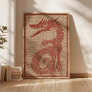 May include: A framed print featuring a red dragon illustration. The dragon has sharp teeth, a long tail, and is set against a textured, off-white background. The artwork is in a wooden frame, suitable for wall decor.
