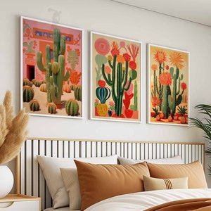 May include: Three framed prints of colorful cactus illustrations. The prints are in gold frames and are hung on a white wall above a bed with brown and white bedding.