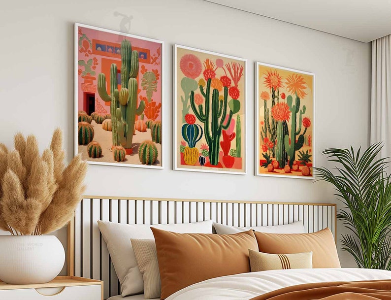May include: Three framed prints of colorful cactus illustrations. The prints are in gold frames and are hung on a white wall above a bed with brown and white bedding.