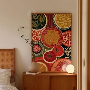 May include: A framed art print featuring a colorful still life of food items. The artwork includes images of tomatoes, oranges, pasta, and other food elements in a vibrant, eye-catching design. The print is displayed on a wooden cabinet.