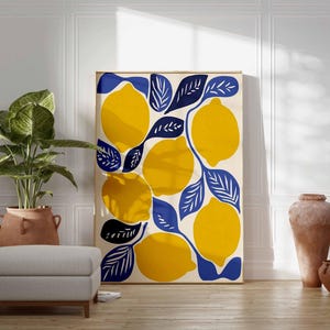May include: A framed art print featuring a vibrant lemon design. The artwork showcases large yellow lemons with blue leaves against a cream background. The print is displayed in a room with a plant, ottoman, and decorative vases.