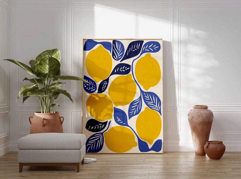 May include: A framed art print featuring a vibrant lemon design. The artwork showcases large yellow lemons with blue leaves against a cream background. The print is displayed in a room with a plant, ottoman, and decorative vases.