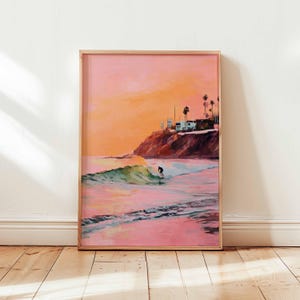 May include: Framed art print depicting a surfer riding a wave at sunset. The artwork features a vibrant color palette of pinks, oranges, and greens, with a coastal scene including a cliffside and palm trees.