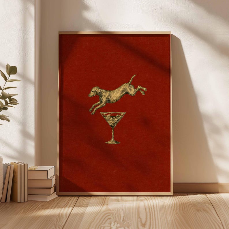 Pu&ograve; includere: Una stampa artistica incorniciata con un cane dorato che salta sopra un bicchiere da martini su uno sfondo rosso intenso. L'opera d'arte ha un'estetica vintage, con una cornice in legno chiaro. La stampa &egrave; esposta su una parete con luce naturale.