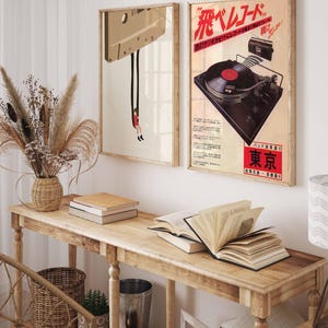 Op de afbeelding: Twee vintage posters op een houten muur. De poster aan de linkerkant toont een cassetteband met een persoon die eraan hangt. De poster aan de rechterkant toont een vintage platenspeler met de tekst "花ベルベット" in rood en zwart.