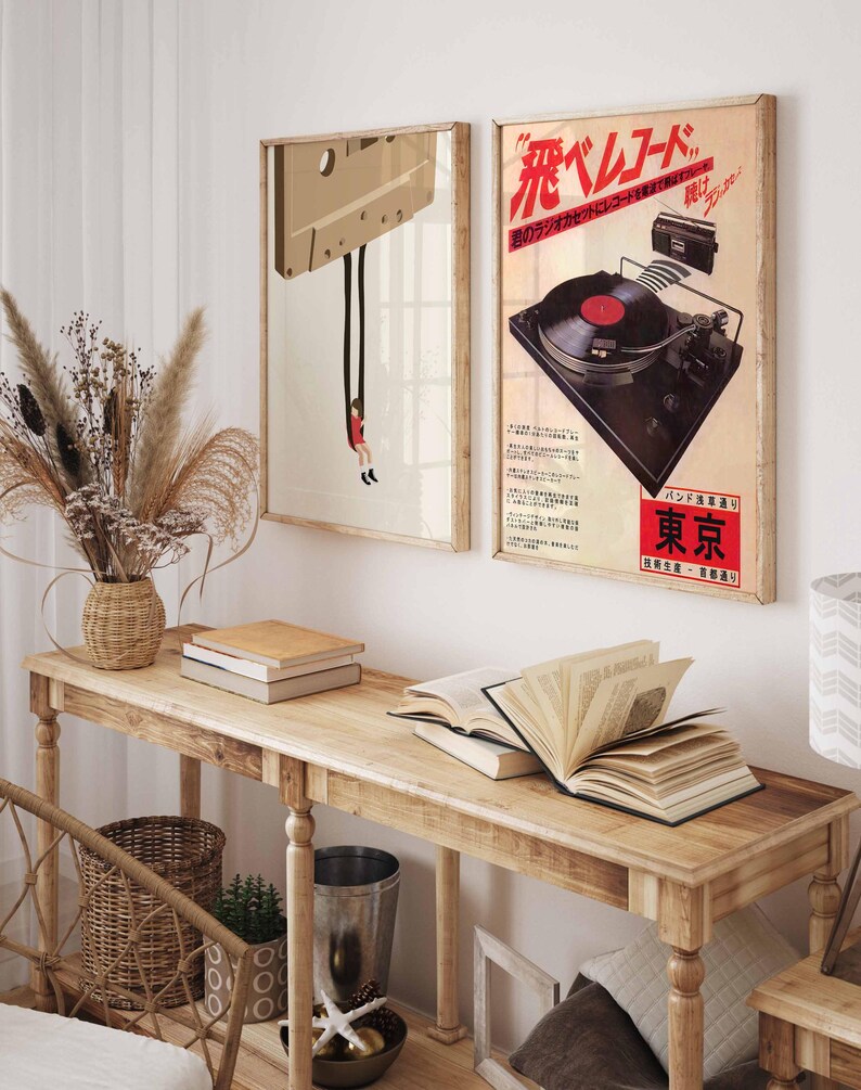 Op de afbeelding: Twee vintage posters op een houten muur. De poster aan de linkerkant toont een cassetteband met een persoon die eraan hangt. De poster aan de rechterkant toont een vintage platenspeler met de tekst "花ベルベット" in rood en zwart.