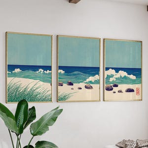 Puede incluir: Conjunto de tres grabados enmarcados que representan una escena de playa. Cada grabado presenta un cielo azul claro, olas oceánicas azul oscuro, arena blanca y hierba verde. Los marcos tienen un acabado dorado.