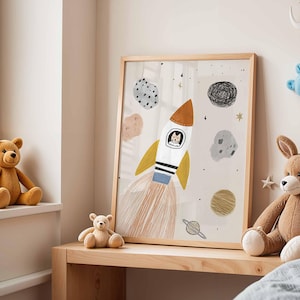 May include: A framed illustration features a rocket ship with a cat pilot, surrounded by planets and stars. The artwork has a light beige background and a wooden frame. The rocket has orange, yellow, white, and blue accents. The artwork is on a wooden shelf.