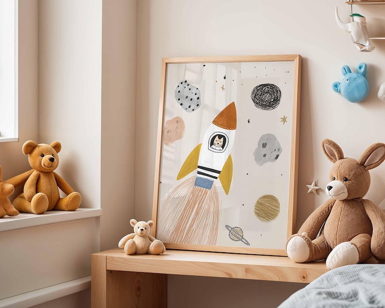 May include: A framed illustration features a rocket ship with a cat pilot, surrounded by planets and stars. The artwork has a light beige background and a wooden frame. The rocket has orange, yellow, white, and blue accents. The artwork is on a wooden shelf.