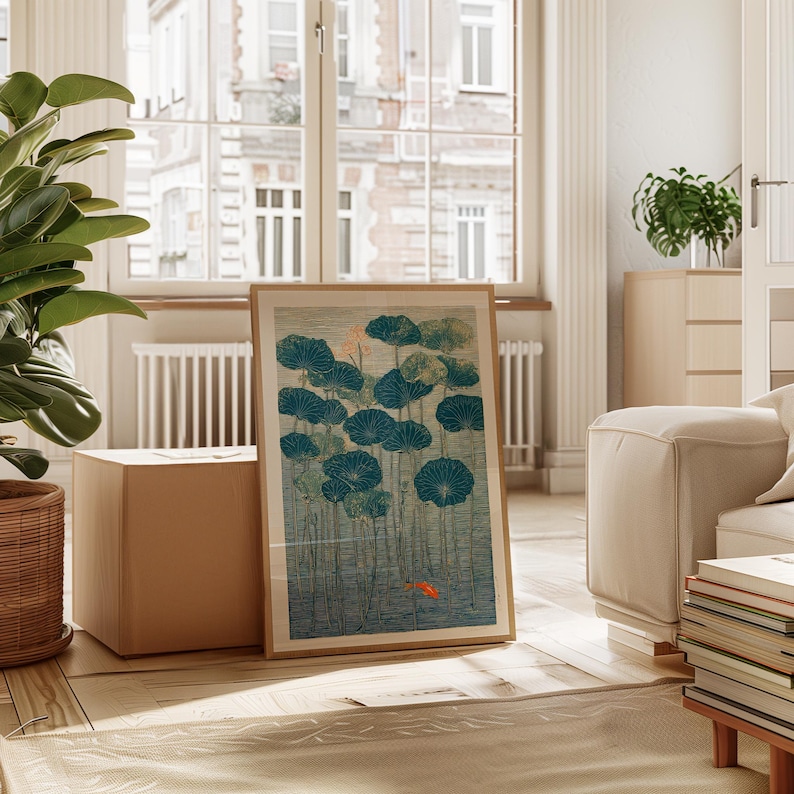 May include: A framed art print featuring a serene pond scene with teal lily pads and a small orange fish. The artwork has a vintage aesthetic, with a light brown wooden frame. The print is displayed in a well-lit living room setting.