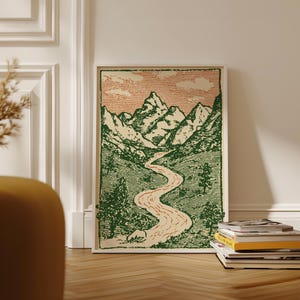 May include: A framed art print featuring a mountain landscape with a winding river. The artwork uses green and peach tones, with a vintage aesthetic. The print is displayed on a wooden floor, leaning against a white wall.
