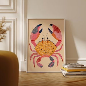 May include: A framed art print featuring a colorful crab illustration. The crab has a yellow body with black dots, pink and red claws, and blue accents. The artwork is displayed on a light beige background.