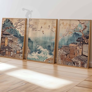 May include: Three framed prints depicting a Japanese scene with traditional houses, cherry blossoms, and birds flying over a blue ocean with waves. The prints are in a light wood frame.