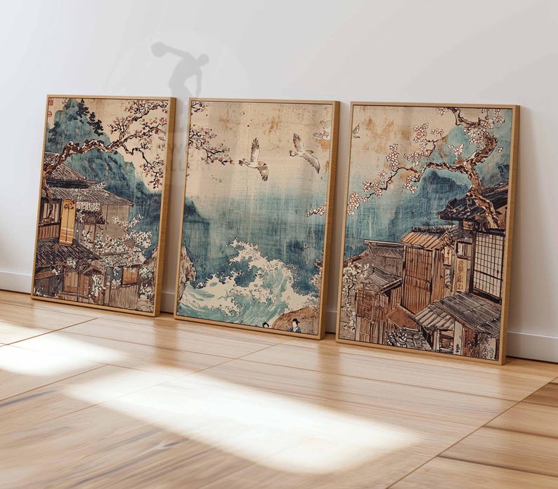 May include: Three framed prints depicting a Japanese scene with traditional houses, cherry blossoms, and birds flying over a blue ocean with waves. The prints are in a light wood frame.