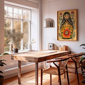 May include: A wooden table with two chairs in a room with a window and a framed print of a colourful illustration of a Russian nesting doll. The print features a woman with a floral design and the text "Matryoshka".