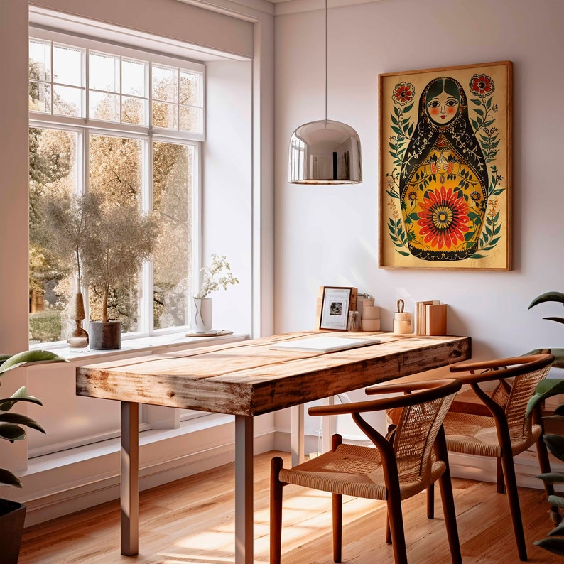 May include: A wooden table with two chairs in a room with a window and a framed print of a colourful illustration of a Russian nesting doll. The print features a woman with a floral design and the text "Matryoshka".