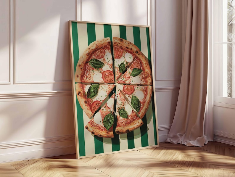 May include: A framed print of a pizza cut into slices, with tomatoes, mozzarella, and basil. The pizza is on a green and white striped background. The frame is leaning against a white wall and wooden floor.