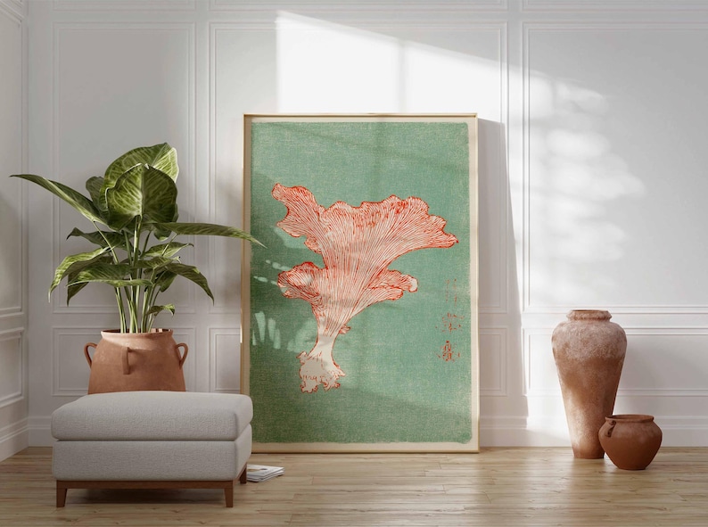 May include: A framed art print featuring a coral-colored mushroom illustration against a muted green background. The artwork is displayed in a room with a potted plant, a gray ottoman, and decorative pottery, creating a serene atmosphere.