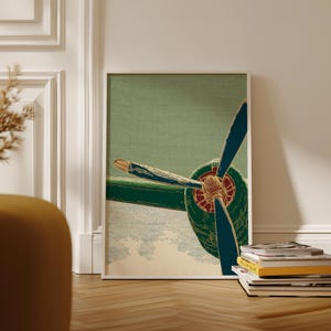 May include: A framed art print showing a close-up of an aircraft propeller. The blades are blue with gold tips, set against a green and beige backdrop. The artwork is displayed on a wooden floor.