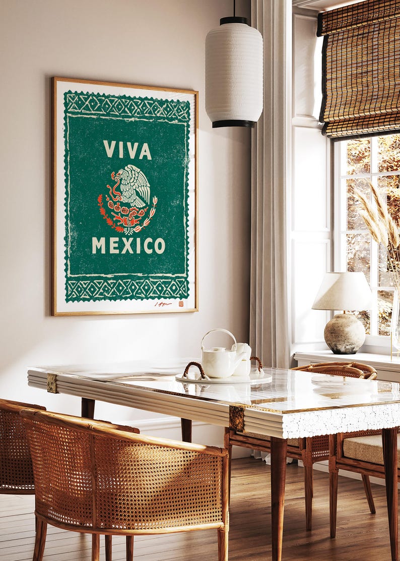 May include: A framed poster with a green background and the words "VIVA MEXICO" in white. The Mexican coat of arms is in the center. The poster is hanging on a wall above a table with woven chairs.